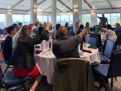 photo of PUC staff Dec 4 PUC All Staff Meeting and Training seated on round tables in a conference room with arms and thumbs up.